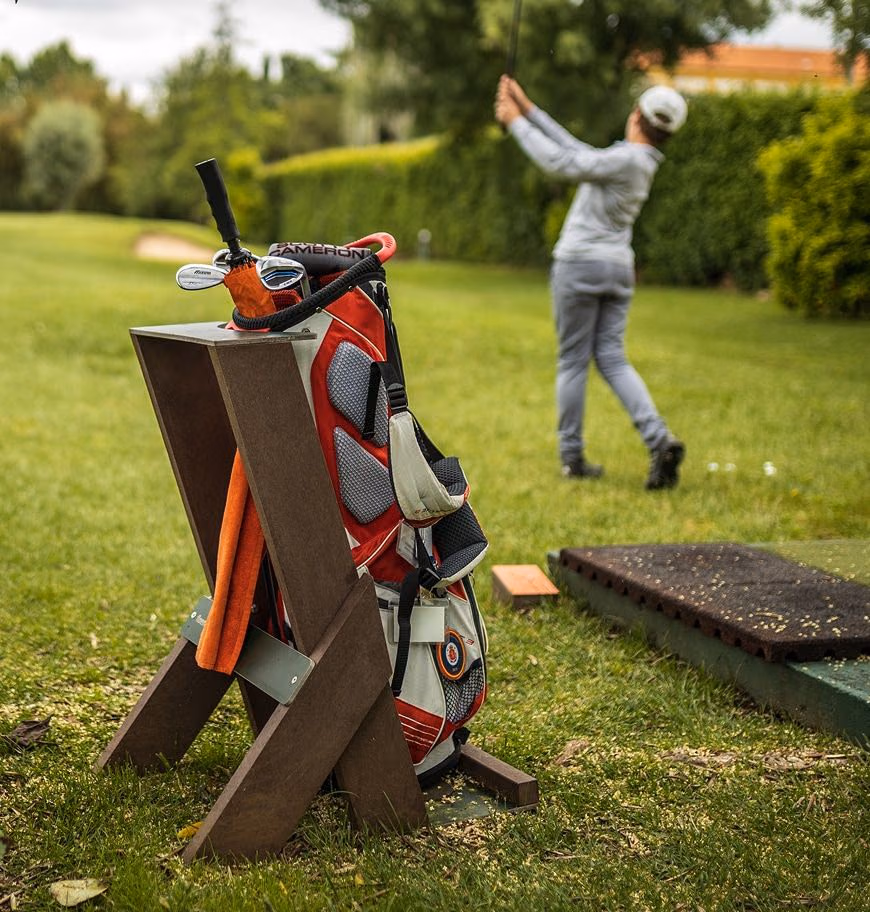 Área de tee de campo de golf com jogador a fazer swing e com o seu saco de tacos de golf no bag stand Royal da Floema Golf, com estrutura em plástico reciclado e HPL+.